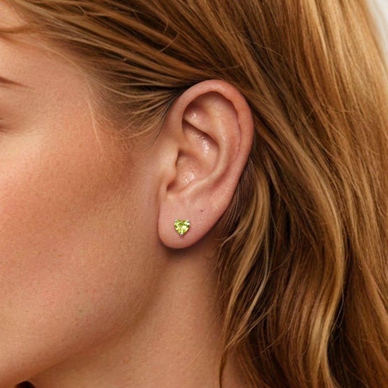 Boucle d'oreille en argent avec une pierre de péridot en forme de cœur vert vif, portée sur l'oreille d'une femme.
