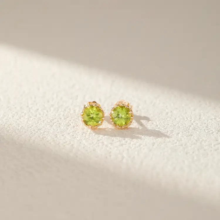 Pair of round peridot stud earrings set in gold-plated silver, with a sun-like serrated bezel.