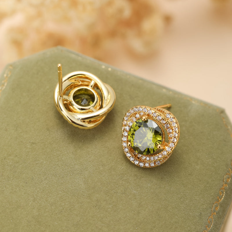 Boucles d'oreilles plaqué or avec une pierre centrale ronde de péridot vert vif, entourée de petites pierres scintillantes, sur un fond vert sapin.