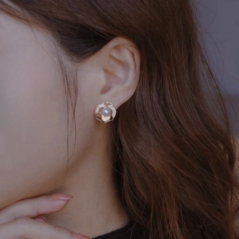 Boucles d'oreilles plaqué or en forme de fleur avec une perle au centre, portées par une femme.