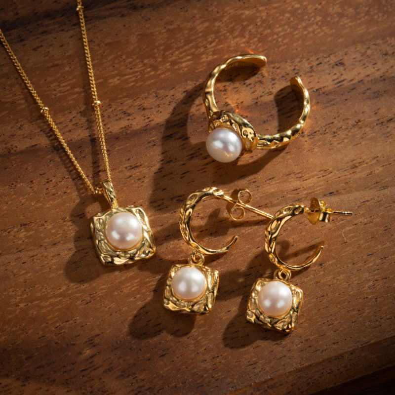 Ensemble de bijoux en argent plaqué or comprenant une paire de boucles d'oreilles pendantes et une bague ornée de perles blanches.