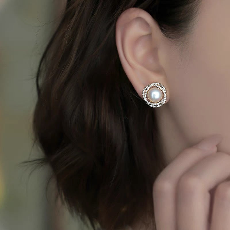 Boucles d'oreilles en argent plaqué or ornées d'une perle centrale entourée de cristaux scintillants, montées sur l'oreille d'une femme.