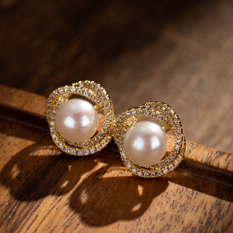 Paire de boucles d'oreilles en argent plaqué or ornées de perles et de zirconiums, sur fond de bois sombre.