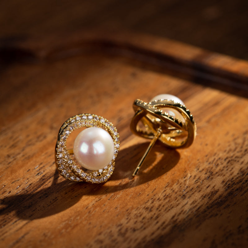 Boucles d'oreilles en argent plaqué or ornées de perles et de petites pierres scintillantes, posées sur un fond en bois sombre.