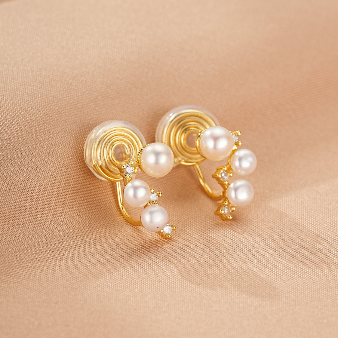 Boucles d'oreilles en perles nacrées et strass, montées sur un support doré en spirale, style élégant et moderne.