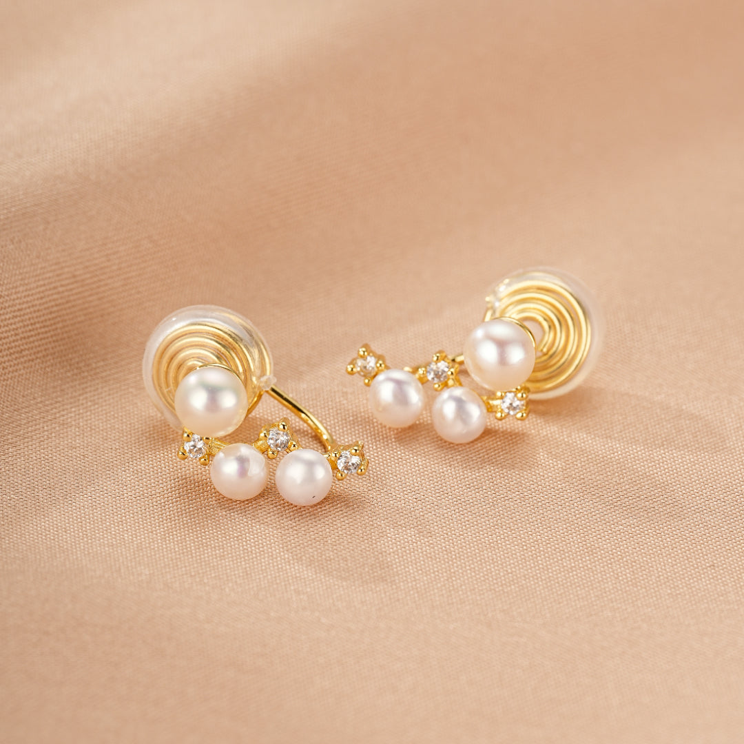 Paire de boucles d'oreilles dorées ornées de petites perles et d'éclats de cristaux, sur un fond beige satiné.
