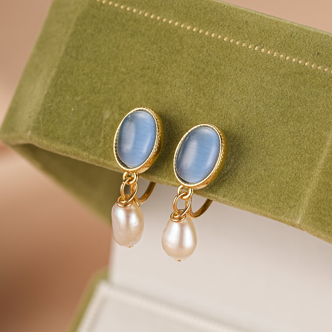 Boucles d'oreilles plaquées or avec une pierre bleue ovale et une perle en forme de gouttelette suspendue.