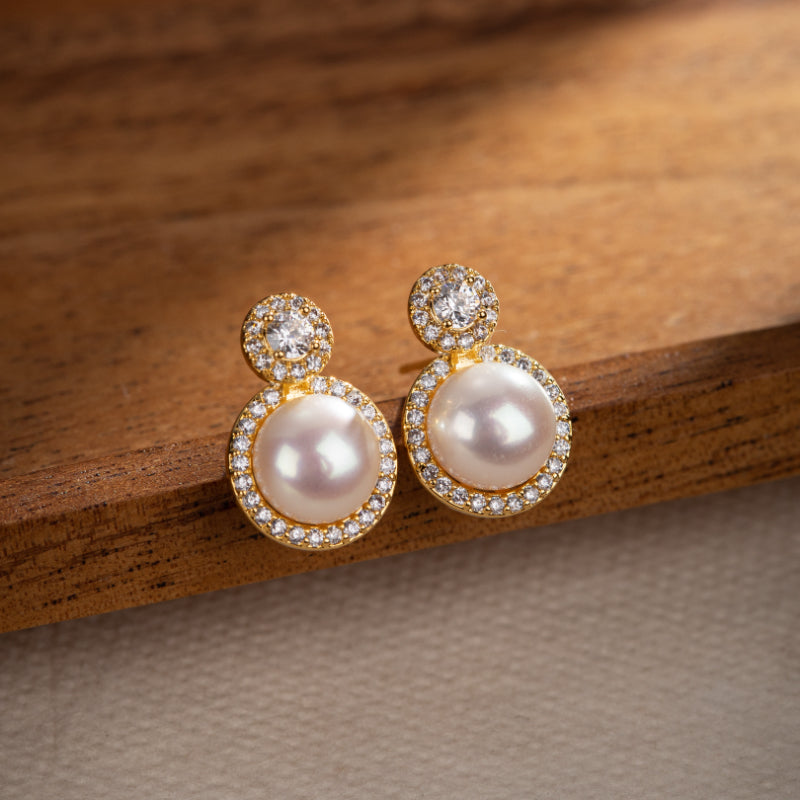 Boucles d'oreilles pendantes en or plaqué serties de perles et de zircons cubiques scintillants sur un fond en bois