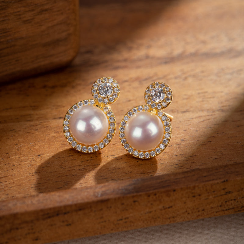 Boucles d'oreilles plaquées or avec perles roses et cristaux, présentées sur un fond en bois.