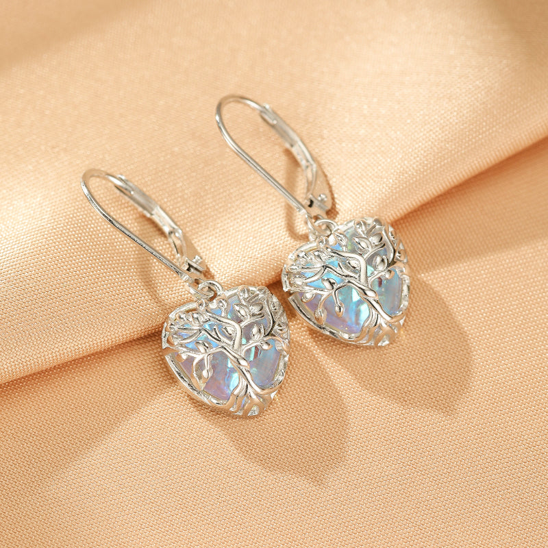Boucles d'oreilles pendantes en argent S925, en forme de cœur ajouré avec un arbre stylisé, ornées d'une pierre de lune irisée aux reflets bleutés.