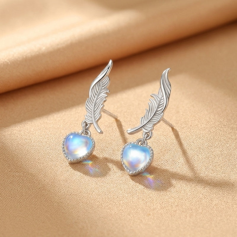 Boucles d'oreilles en argent avec pendentifs en forme de cœur en pierre de lune et motif de plume céleste.