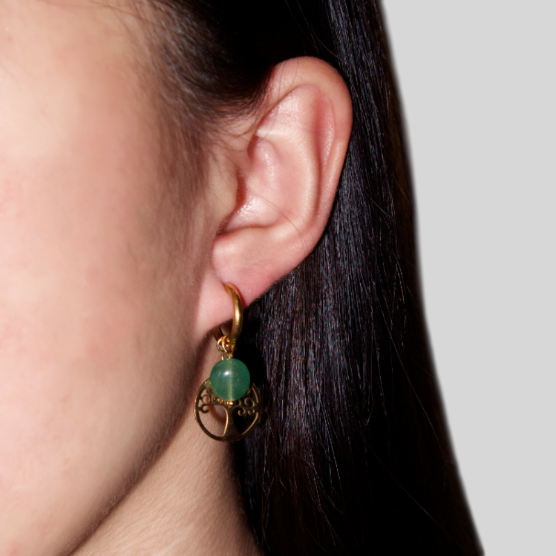 Boucle d'oreille plaquée or avec une pierre naturelle verte et un pendentif Arbre de Vie, porté à l'oreille d'une femme.