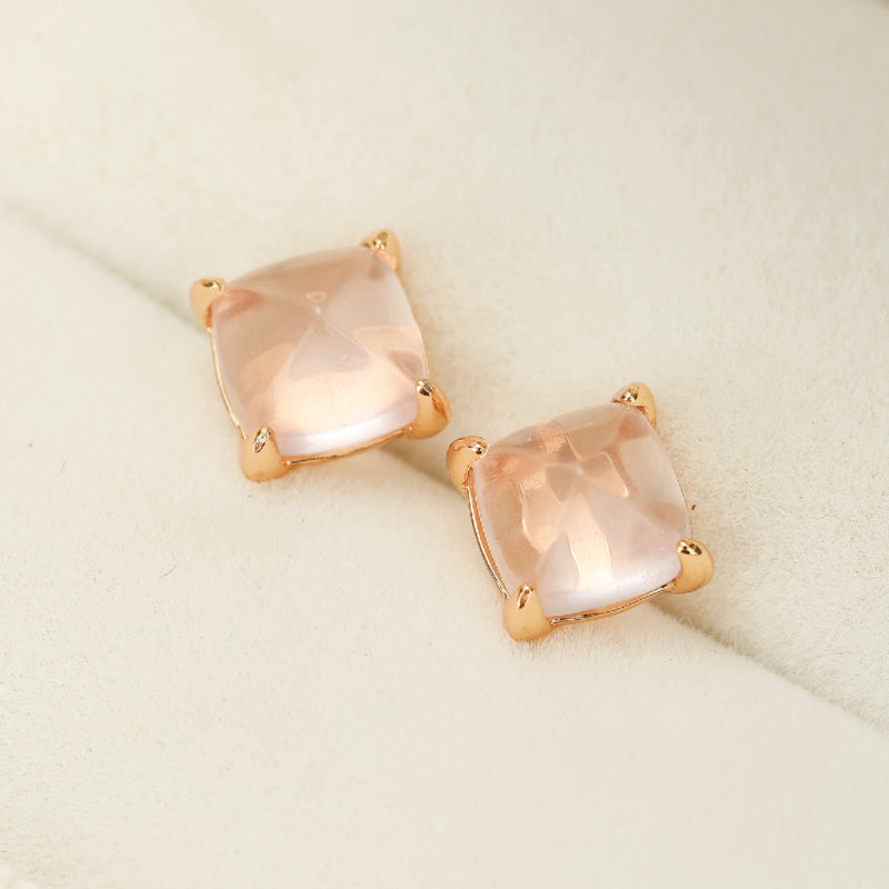 Boucles d'oreilles carrées en quartz rose clair avec monture plaquée or, gros plan sur fond crème