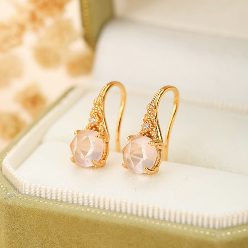 Boucles d'oreilles pendantes en argent plaqué or ornées de quartz rose facetté et de petits diamants, présentées dans un écrin vert.