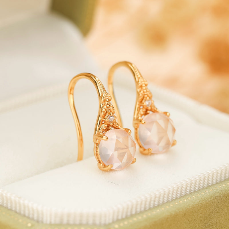 Boucles d'oreilles pendantes en argent plaqué or ornées de quartz rose facetté et de petites pierres d'accent, présentées dans un écrin.