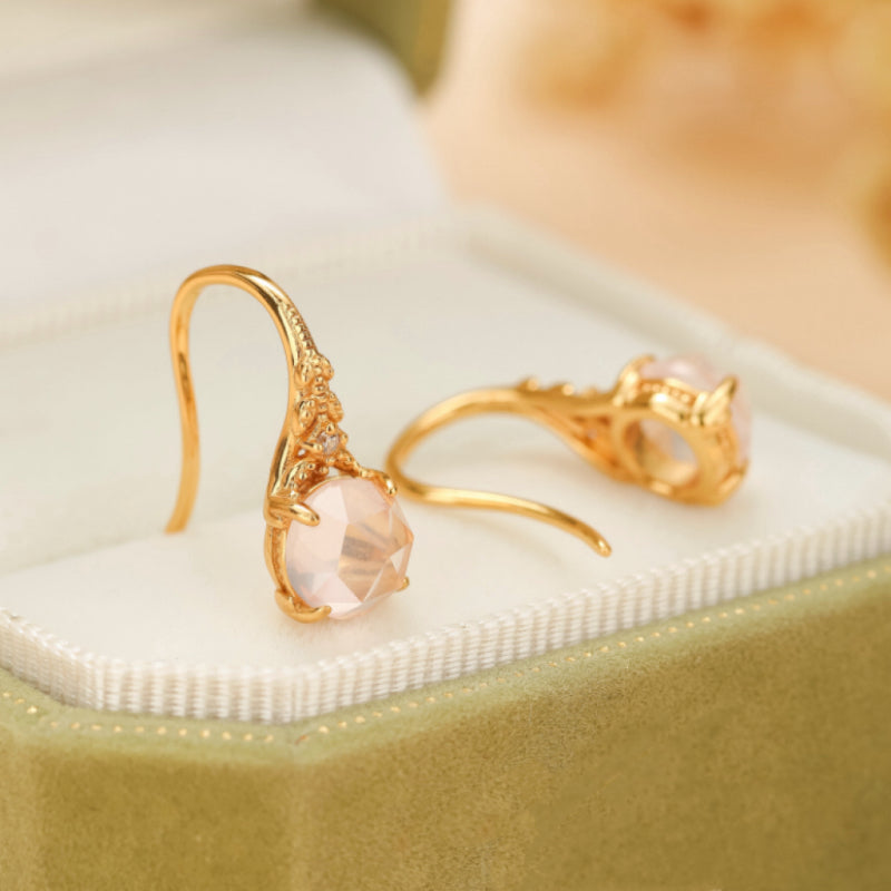 Paire de boucles d'oreilles pendantes en argent plaqué or ornées de quartz rose facetté et de petites pierres scintillantes, présentées dans un écrin vert.