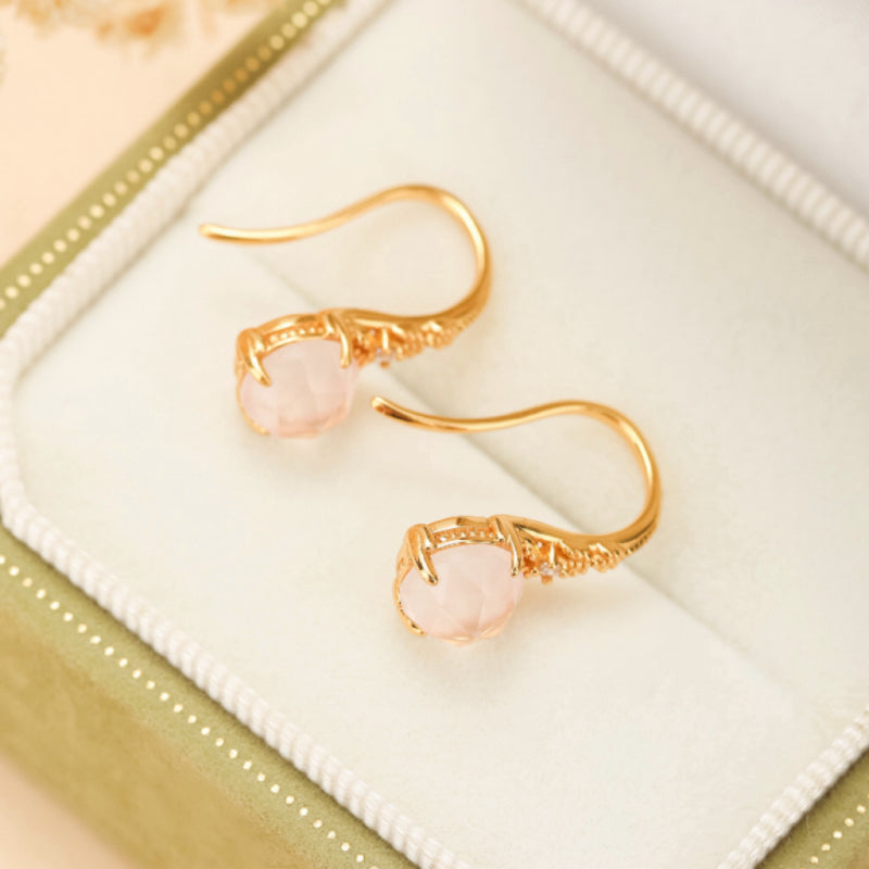 Paire de boucles d'oreilles pendantes en argent plaqué or ornées de quartz rose facetté, présentées dans un écrin vert.