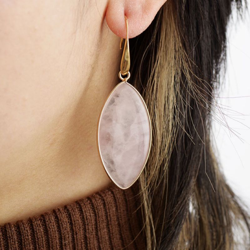 Boucle d'oreille longue en quartz rose ovale avec monture dorée, portée par une femme.
