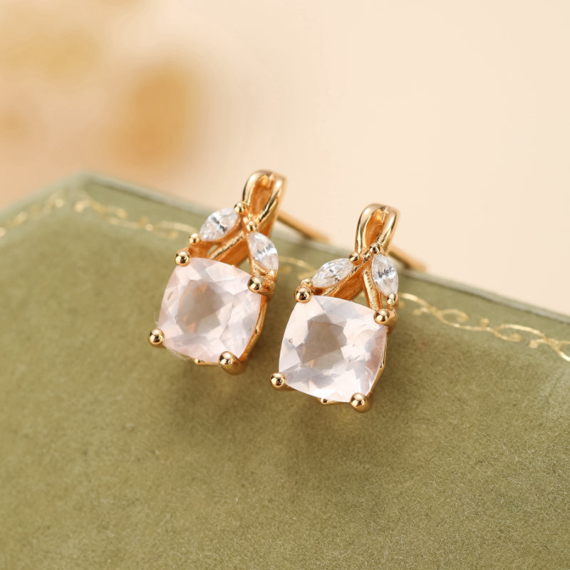 Boucles d'oreilles ornées de quartz rose carré et de petites feuilles en argent plaqué or, sur un fond vert.