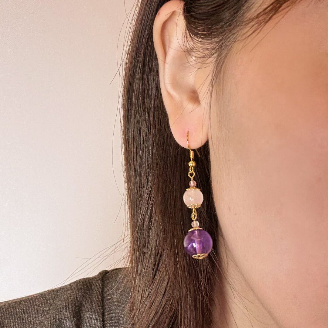 Boucles d'oreilles "Plongée Éther" avec une perle ronde de quartz rose et une perle ronde d'améthyste, montées sur un fil doré avec de petites perles roses.