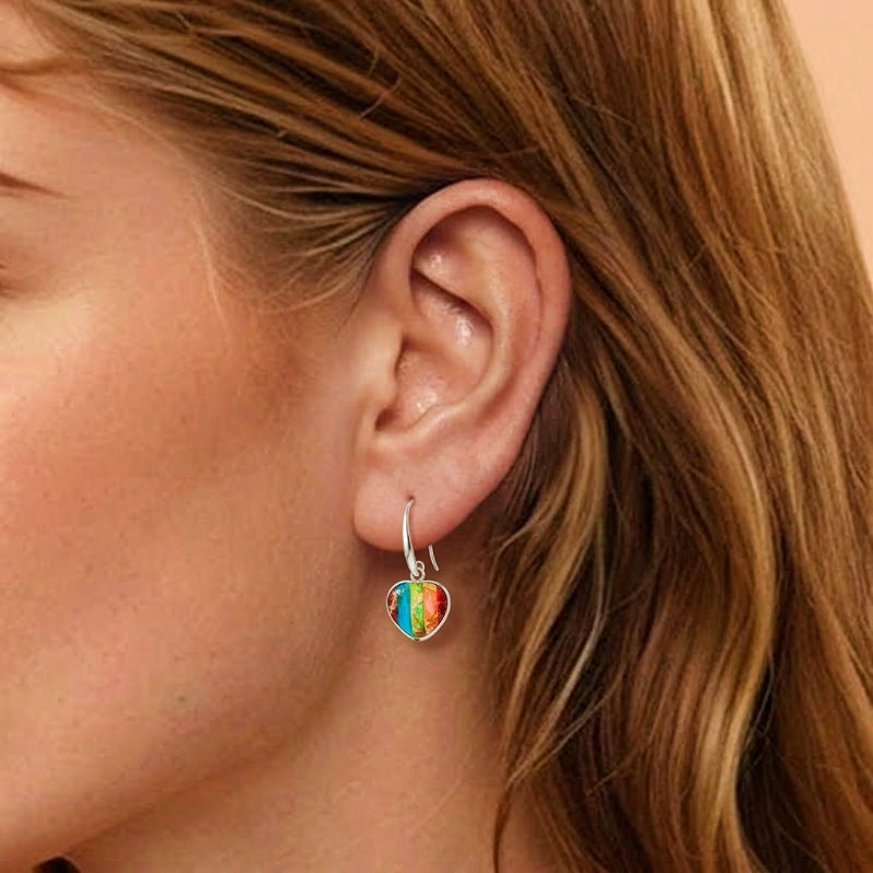 Boucle d'oreille Regalite - Astralis Cœur avec un pendentif cœur multicolore rayé, porté à l'oreille d'une femme aux cheveux blonds.