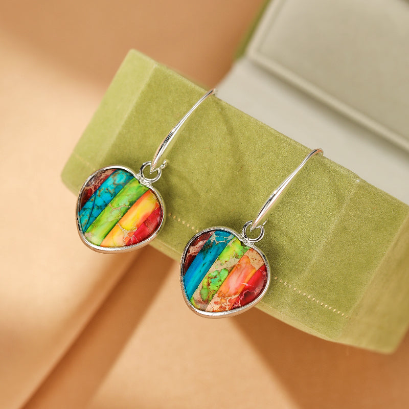 Paire de boucles d'oreilles cœur en pierre naturelle multicolore rayée, montées sur un fermoir argenté, présentées dans un écrin vert.