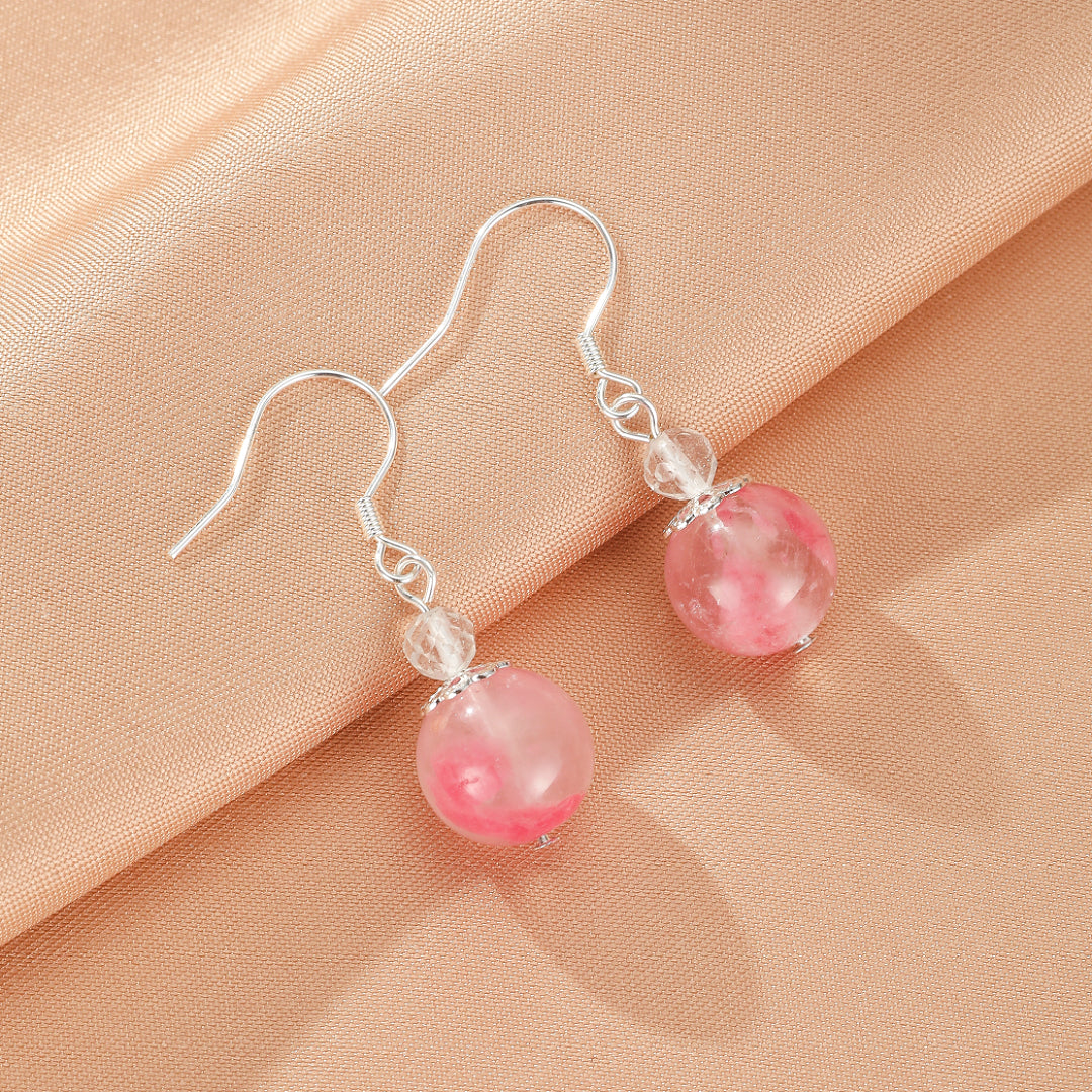 Boucles d'oreilles pendantes en argent ornées de perles rondes roses et de petites perles transparentes, sur un fond satiné rose poudré.