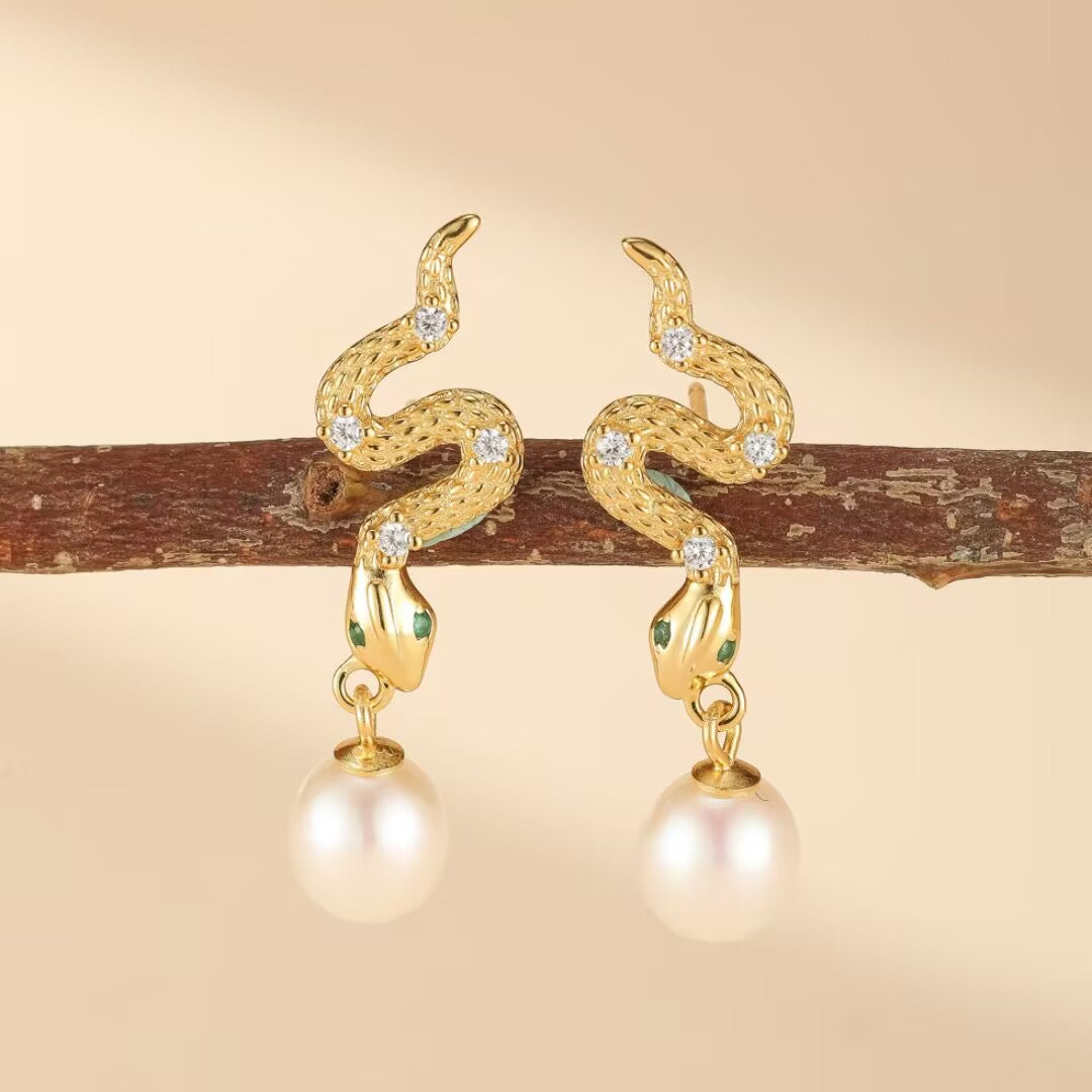 Paire de boucles d'oreilles serpent dorées ornées de zircons blancs et de perles nacrées, posées sur une branche.
