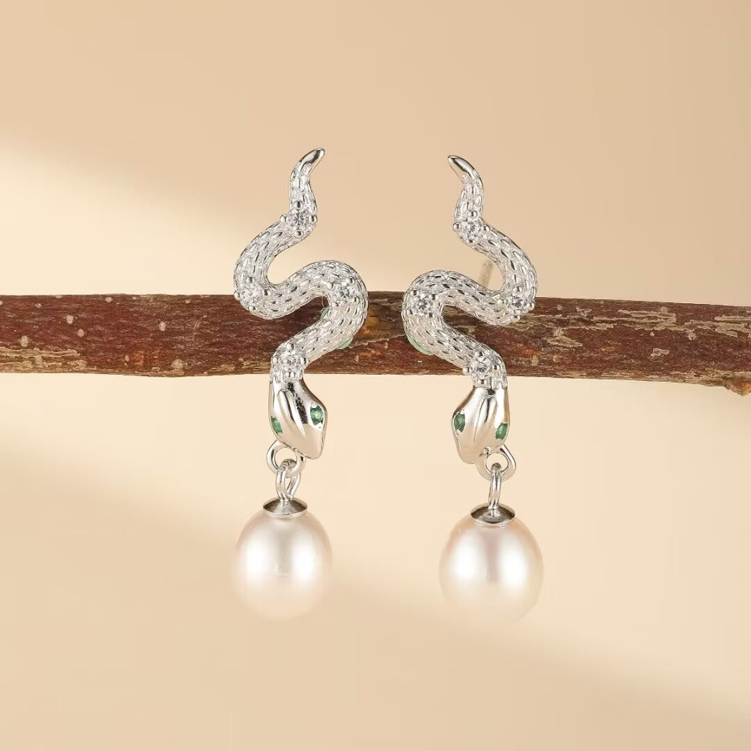 Paire de boucles d'oreilles serpent en argent 925 ornées de perles blanches et d'yeux verts, suspendues à une branche.