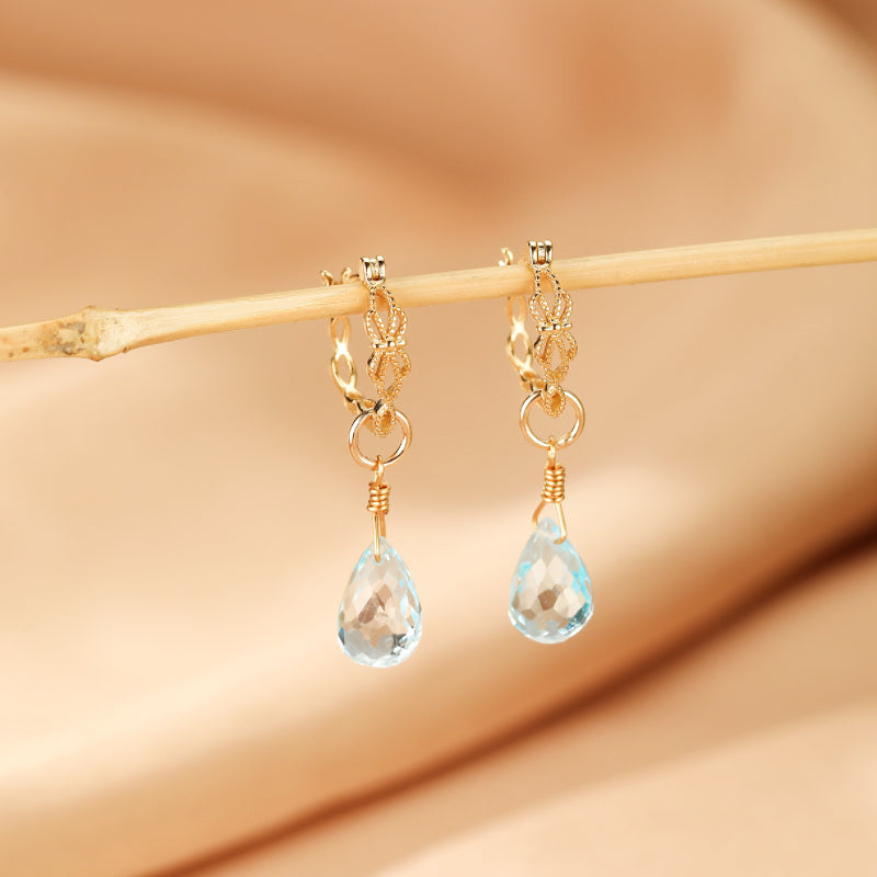 Boucles d'oreilles "Goutte de Sérénité" en argent plaqué or avec topazes bleues naturelles taillées en goutte suspendues à des créoles fines ornées.