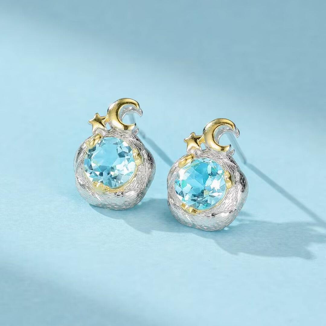 Boucles d'oreilles en argent 925 ornées de topazes bleues rondes, serties sur un motif de croissant de lune et d'étoile dorés.