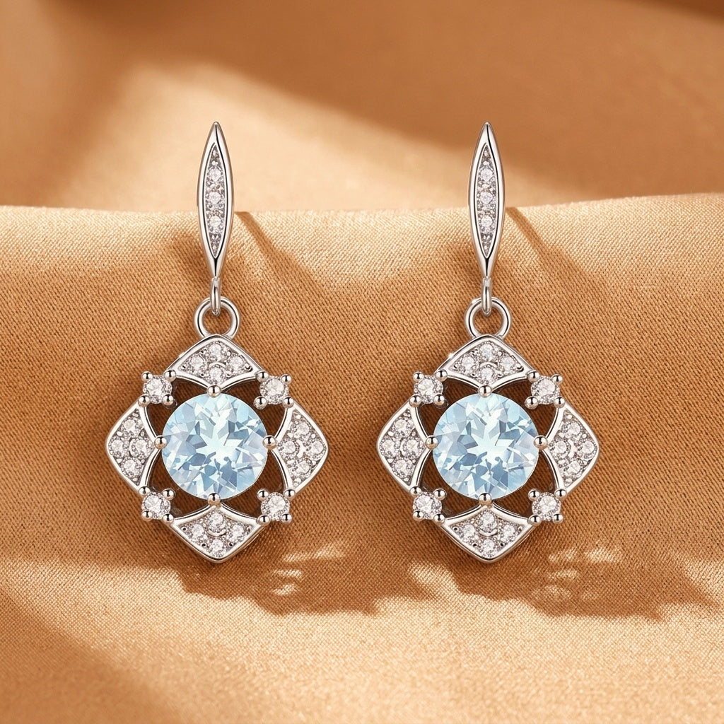 Boucles d'oreilles pendantes en argent avec une topaze bleu clair centrale entourée de petites pierres scintillantes, motif floral stylisé.