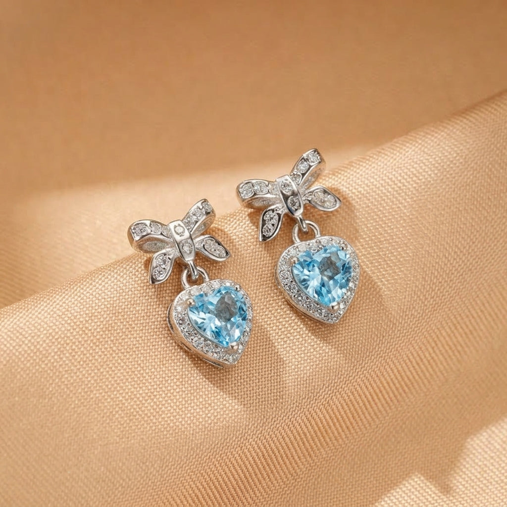 Boucles d'oreilles en argent ornées de topazes bleues en forme de cœur et de nœuds en argent sertis de petites pierres scintillantes.