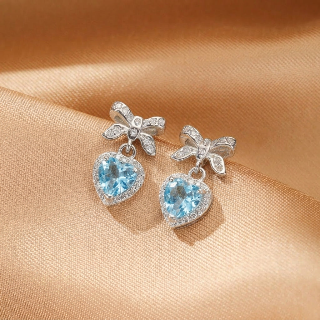 Boucles d'oreilles nœud d'amour en argent avec topaze bleue en forme de cœur et cristaux scintillants.