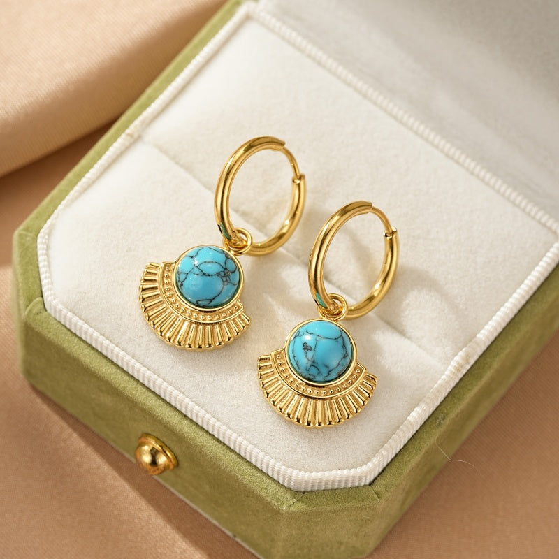 Boucles d'oreilles créoles dorées ornées d'une pierre turquoise et d'un pendentif éventail texturé, présentées dans un écrin vert.