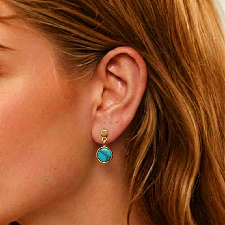 Boucle d'oreille plaqué or avec une turquoise ronde au centre, portée à l'oreille.