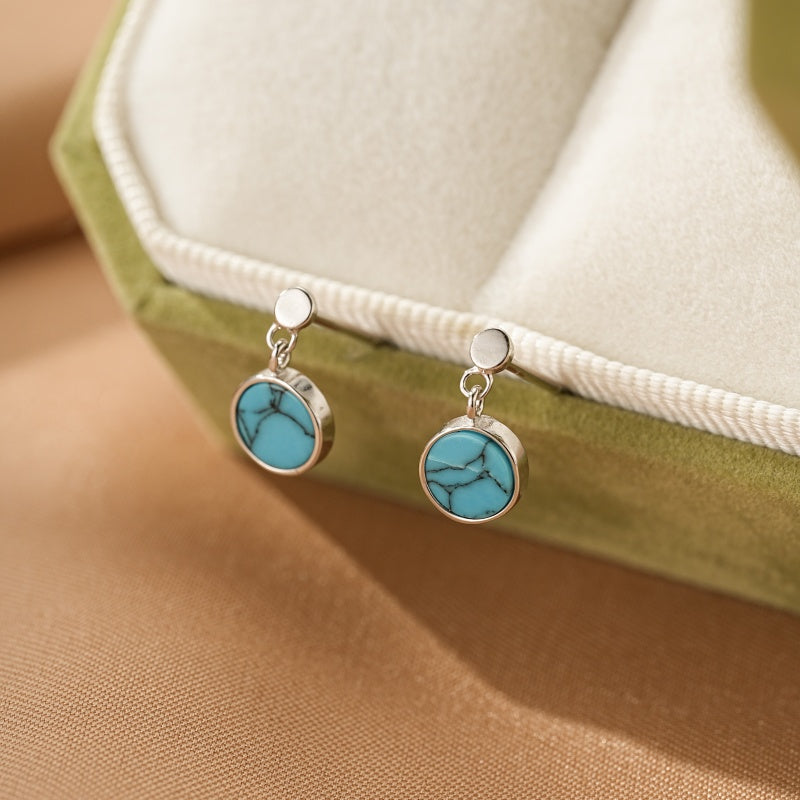 Boucles d'oreilles pendantes en argent avec une turquoise ronde et veinée, montées sur un fermoir discret.