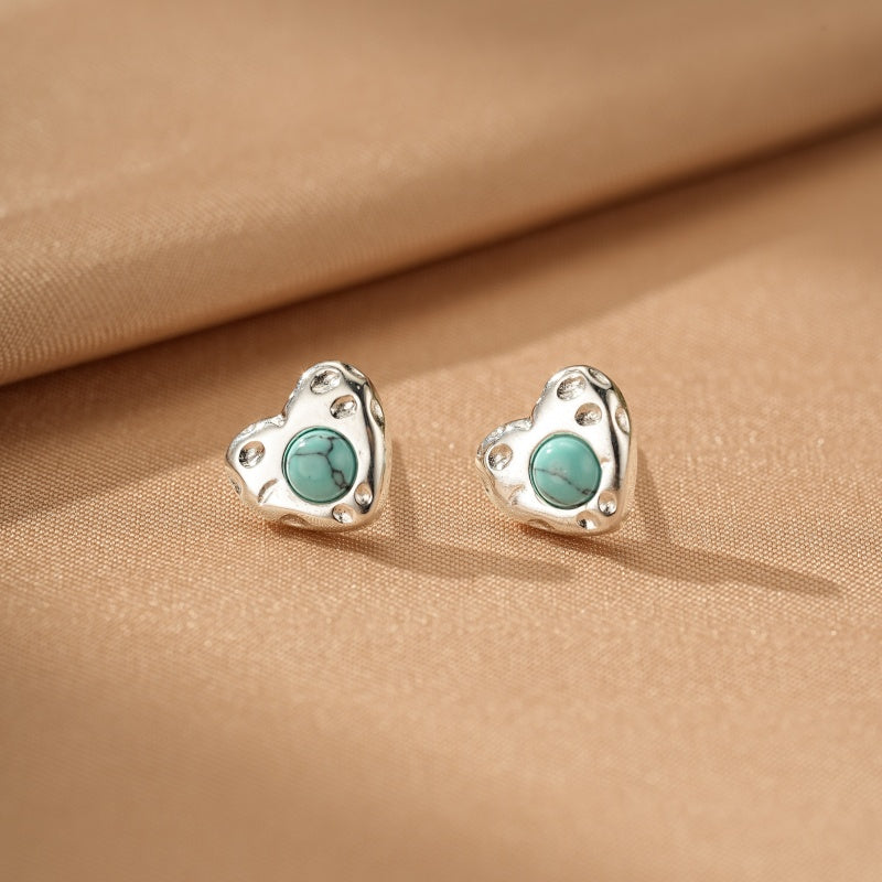 Boucles d'oreilles cœur en argent avec une turquoise au centre, sur fond beige.