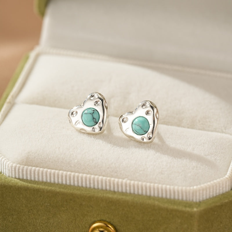 Boucles d'oreilles cœur en argent avec une turquoise centrale, présentées dans une boîte à bijoux verte.