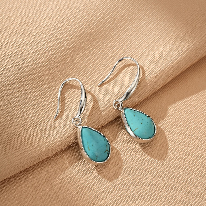 Boucles d'oreilles pendantes en argent avec des pierres turquoise en forme de goutte, sur fond beige