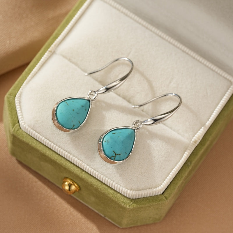 Boucles d'oreilles pendantes avec une turquoise en forme de goutte et une monture argentée, présentées dans une boîte à bijoux verte.