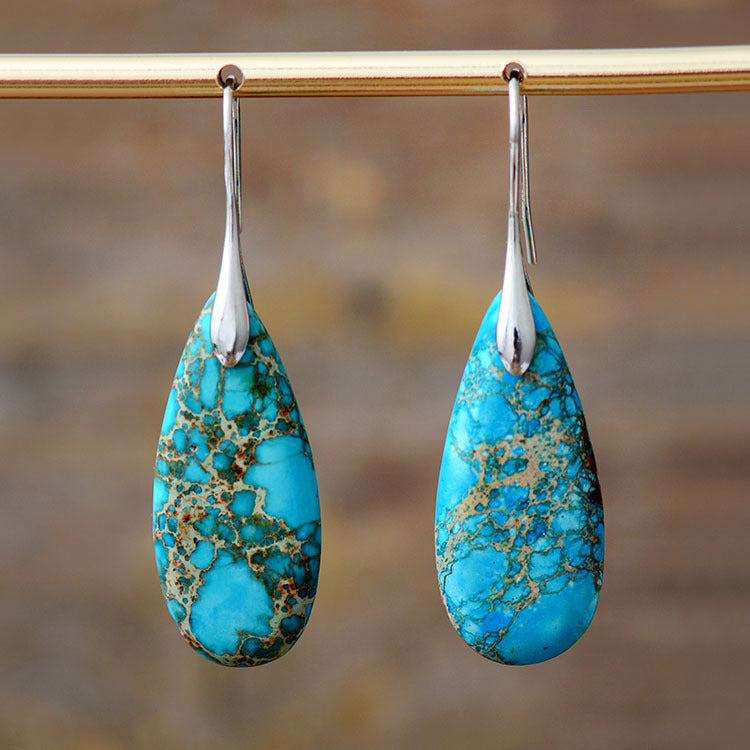 Boucles d'oreilles majestueuses en turquoise avec des inclusions dorées, suspendues à des crochets argentés.