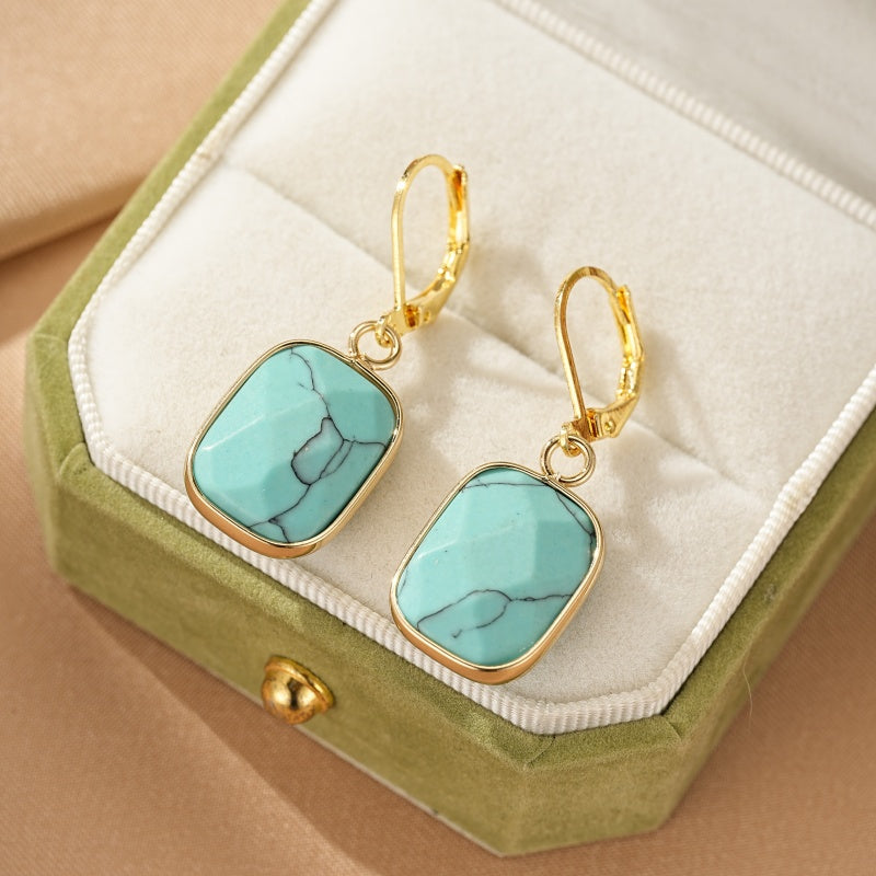 Boucles d'oreilles rectangulaires en turquoise avec monture dorée, présentées dans une boîte à bijoux verte.