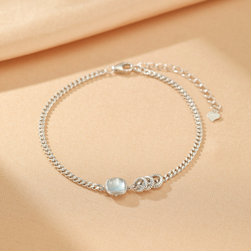 Bracelet en argent avec une pierre carrée bleu clair et trois anneaux décoratifs, fermoir mousqueton et pendentif cœur.
