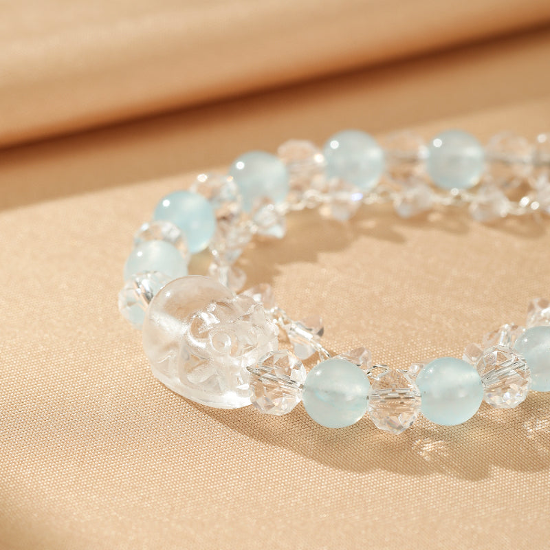 Bracelet artisanal fait à la main avec des perles rondes d'aigue-marine bleu pâle et des cristaux de roche transparents, orné d'une petite sculpture transparente.