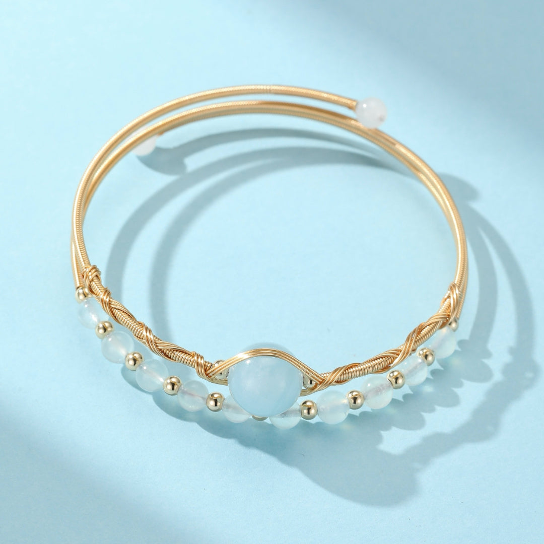 Bracelet jonc doré avec des perles d'aigue-marine et de petites perles dorées, sur fond bleu clair.
