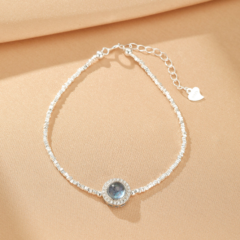 Bracelet "Souffle Marin" en argent avec une pierre d'aigue-marine bleue centrale entourée de petits cristaux scintillants et une chaîne fine ornée de perles.