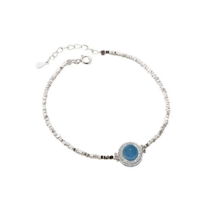 Bracelet en argent avec une pierre d'aigue-marine bleue ronde au centre, orné de petites pierres scintillantes et d'une chaîne fine.