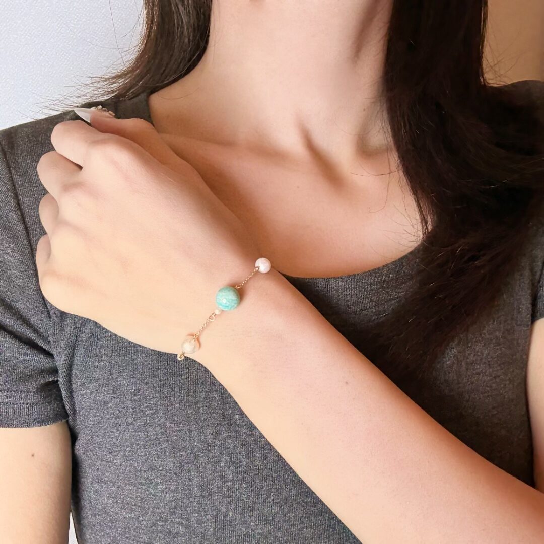 Bracelet fin en or rose orné d'une perle d'amazonite turquoise et de perles nacrées, porté au poignet d'une femme.