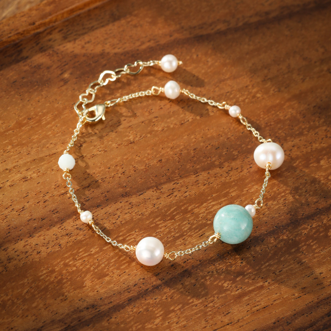 Bracelet délicat en or avec une pierre d'amazonite bleue et de petites perles blanches nacrées, posé sur un fond en bois sombre.